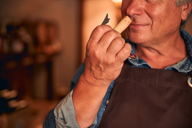 Close up of man in apron sentant le liège de boisson alcoolisée dans la cave à vin