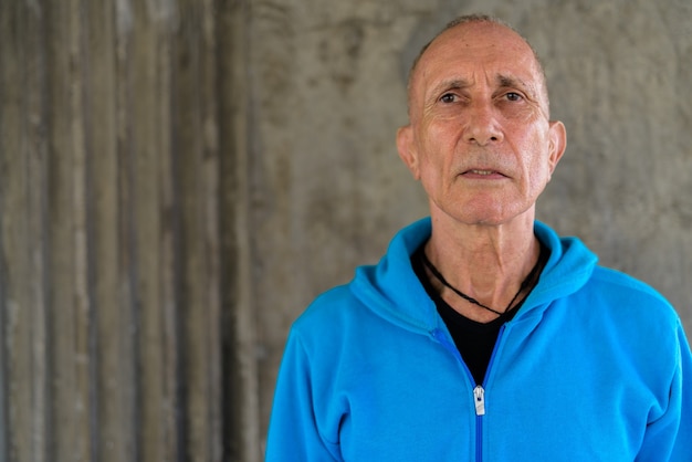 Close up of senior man wearing blue hoodie contre le vieux mur de béton