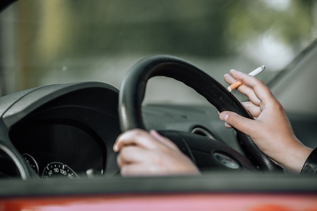 Close up of woman hand smoking cigarette à l'intérieur de la voiture tout en conduisant un véhicule