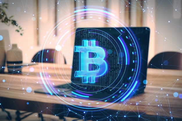 Close-up d'un ordinateur portable avec un hologramme créatif de bitcoin sur un fond flou du bureau de bureau Crypto banque en ligne transformation numérique et concept de finance Double exposition