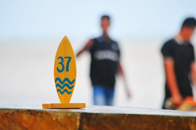 Photo close-up d'un panneau sur du bois contre des hommes qui marchent sur la plage