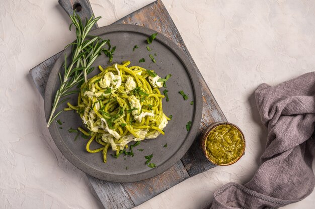 Close up pâtes au pesto, fromage stracciatella et persil servi sur plaque en céramique grise sur bois