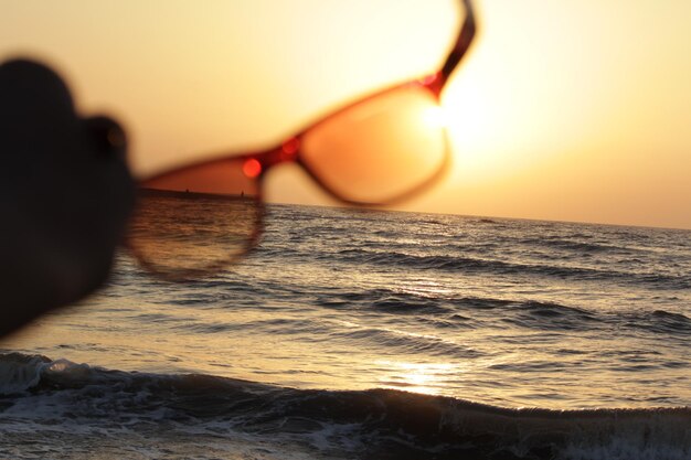 Photo close-up d'une personne en silhouette sur la plage contre le ciel au coucher du soleil