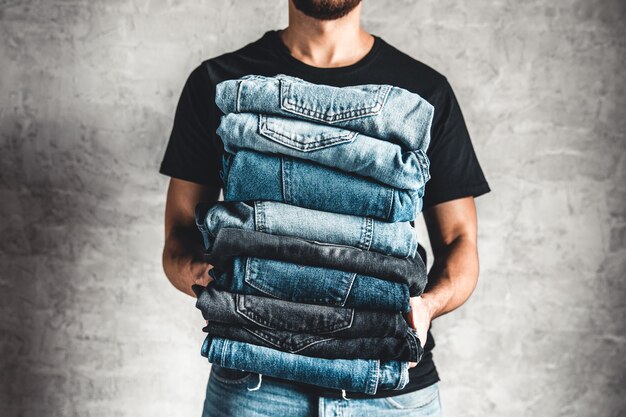 Close up pile de jeans bleu denim plié à la main sur fond de mur gris, espace copie