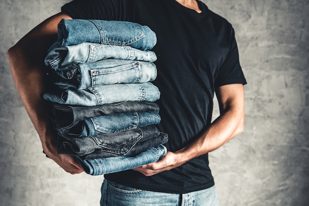 Close up pile de jeans bleu denim plié à la main sur fond de mur gris, espace copie