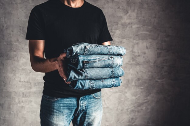 Close up pile de jeans bleu denim plié à la main sur fond de mur gris, espace copie