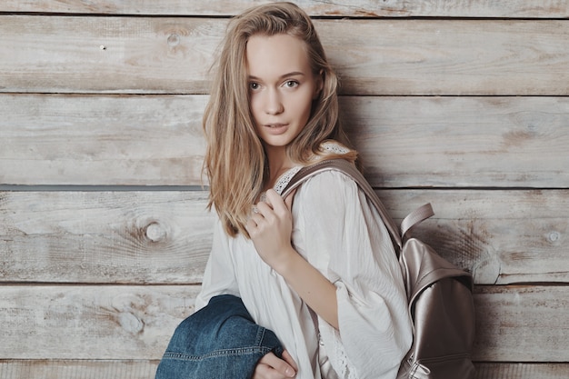 Close up portrait blonde jeune fille avec sac à dos argenté sur mur en bois