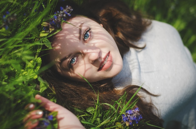 Close up portrait de jeune fille souriante aux yeux bleus, couché sur l'herbe dans le jardin.