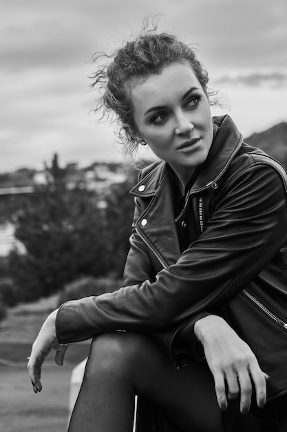 Close-up portrait noir-blanc de mannequin fille en veste noire avec maquillage regarde au loin