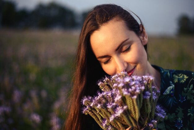 Close-up Portrait of brunette in a floral meadow détient d'être des fleurs sauvages fraîches à l'écoute de l'arôme