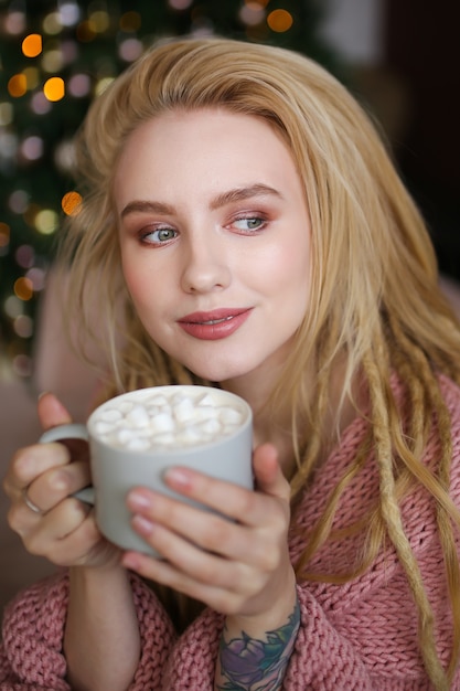 Close-up portrait of dreaming happy girl avec des dreadlocks tenant une tasse de cacao avec des guimauves