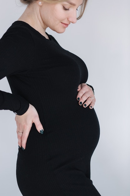 Close up portrait of gogreous enceinte femme en robe bkack tenir sa main sur le ventre et regarde vers le bas