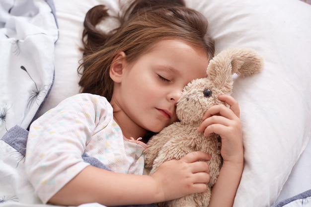 Close up portrait of little girl hugging her teddy bear et être heureux, se reposer après une journée intéressante à kinder garten