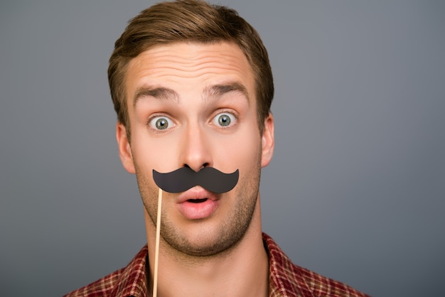 Close up portrait of surpris funny man holding paper moustache
