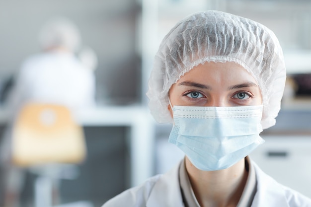 Close up portrait of young female medic portant un masque facial et regardant la caméra tout en travaillant en laboratoire, copiez l'espace