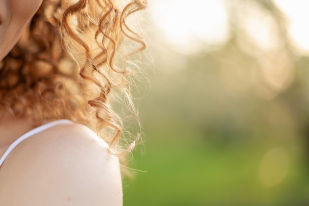 Close up portrait of young smiling attractive woman with curly hair in green flowering spring park