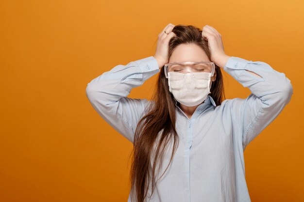 Close-up portrait of young woman on yellow orange wall in protection medical mask