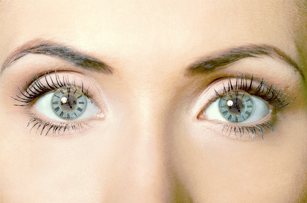 Close up portrait of young woman with clocks at eye looking at camera