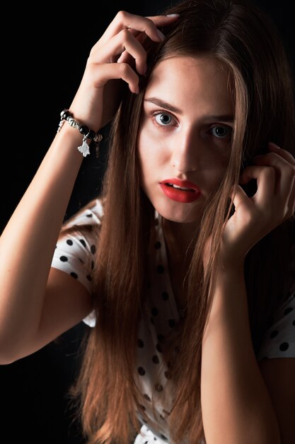 Close-up portrait en studio d'une jeune fille aux cheveux longs et lèvres rouges contre le noir.