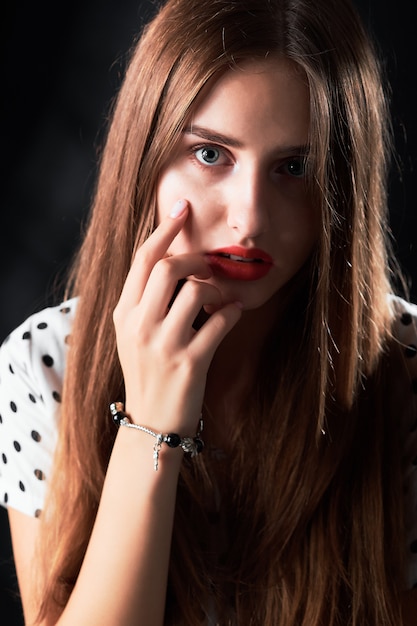Close-up portrait en studio d'une jeune fille aux cheveux longs et lèvres rouges contre le noir.