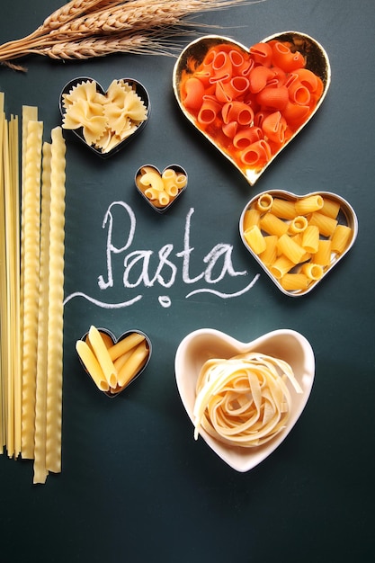 Photo close-up de récipients en forme de cœur avec des pâtes crues et du texte sur fond noir