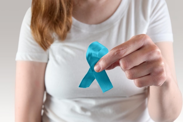 Close-up d'un ruban de sensibilisation teal tenu par une jeune femme caucasienne pour le mois de sensibilisation au cancer du col de l'utérus