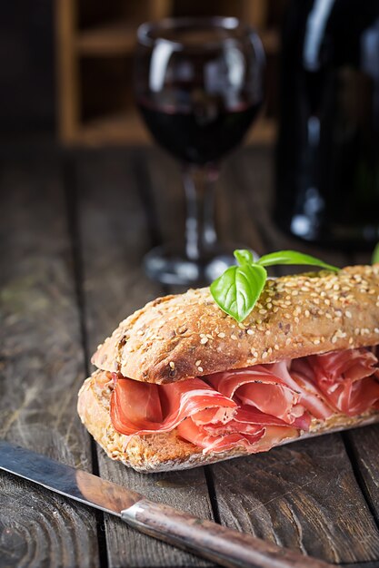 Close up sandwich ciabatta avec jambon serrano et basilic, sur une surface en bois