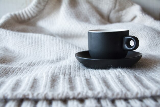 Close-up tasse noire avec café sur pull gris en texture de laine naturelle