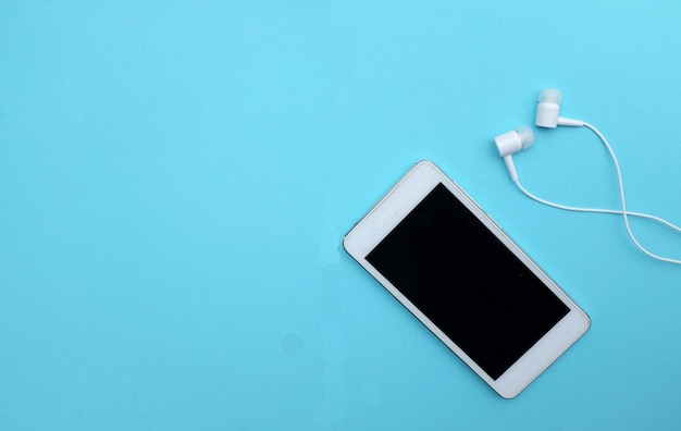 Close-up d'un téléphone intelligent par des écouteurs dans l'oreille sur un fond bleu