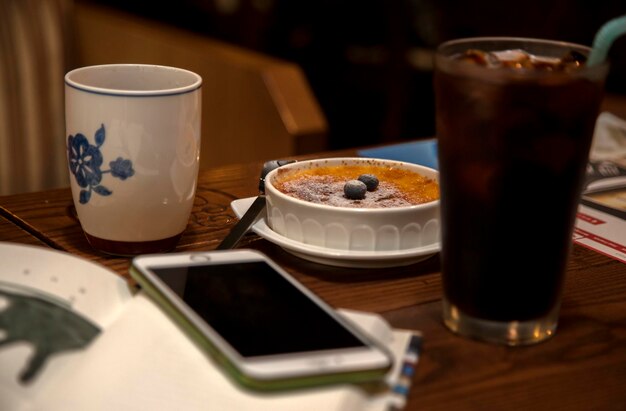 Photo close-up d'un téléphone portable avec des boissons et une tarte sur une table en bois