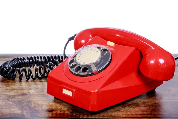 Photo close-up d'un téléphone rotatif rouge sur une table en bois sur un fond blanc