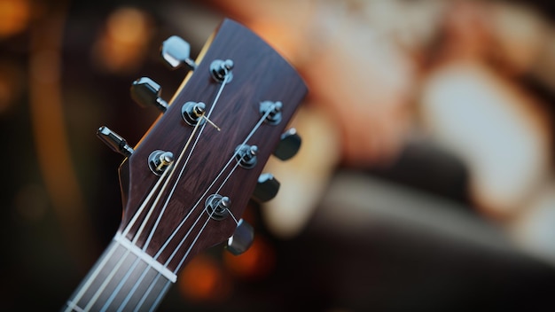 Close-up d'une tête de guitare acoustique La tête de la guitare est en bois avec des accents argentés Derrière lui était une main jouant d'une guitare électrique