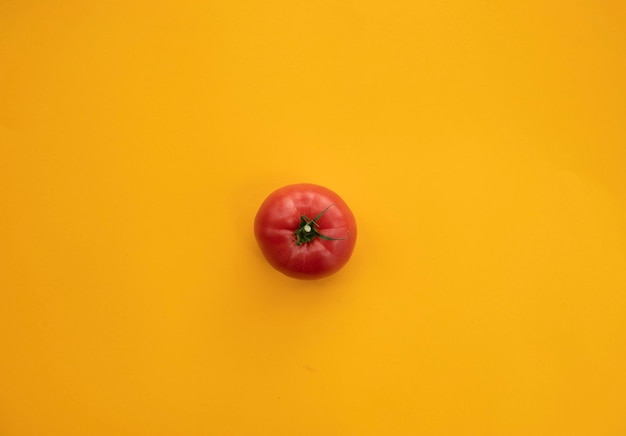 Close up tomate mûre sur fond jaune vif vue de dessus plat poser. Abstrait d'été à la tomate