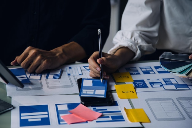 Close up ux développeur et ui concepteur brainstorming sur l'interface d'application mobile wireframe conception sur la table avec le client breif et le code couleur au bureau moderne agence de développement numérique créatif