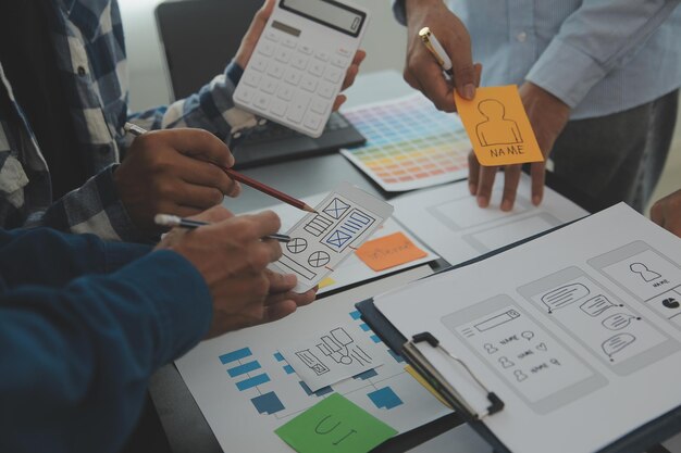 Close up ux développeur et ui concepteur brainstorming sur l'interface d'application mobile wireframe conception sur la table avec le client breif et le code couleur au bureau moderne agence de développement numérique créatif