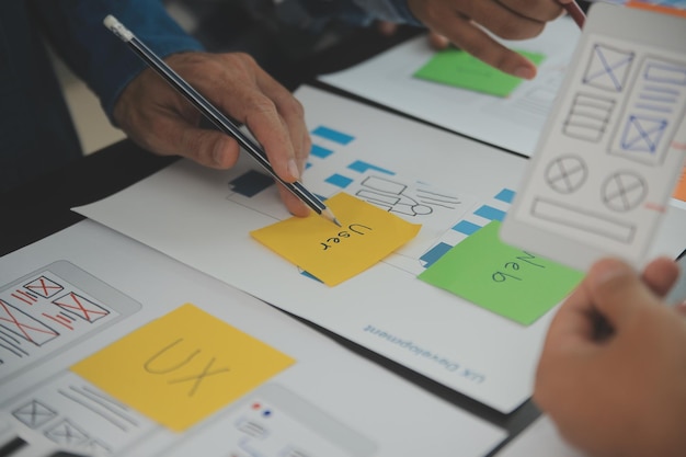 Close up ux développeur et ui concepteur brainstorming sur l'interface d'application mobile wireframe conception sur la table avec le client breif et le code couleur au bureau moderne agence de développement numérique créatif