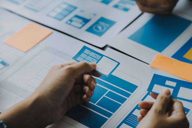 Photo close up ux développeur et ui designer brainstorming sur l'interface d'application mobile wireframe design sur la table avec le client breif et le code couleur au bureau moderne agence de développement numérique créatif