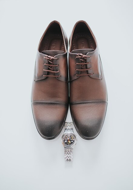 Close-up vertical des chaussures et de la montre d'un homme sur un fond blanc