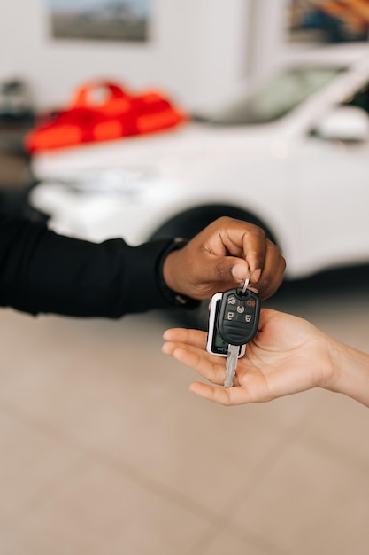 Close-up vertical coupé de l'acheteuse inconnaissable recevant la clé de la voiture et les salutations du concessionnaire d'automobiles afro-américain masculin lors de l'achat d'une nouvelle voiture dans le concessionnaire