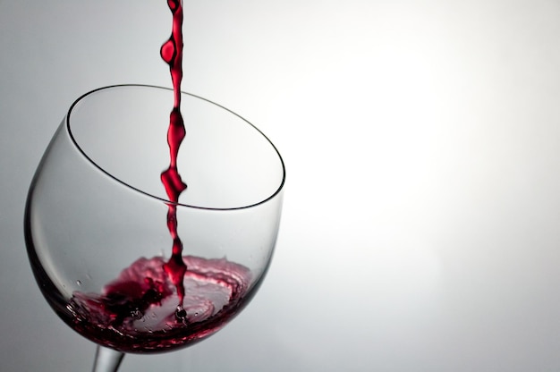 Close-up d'un vin rouge versé dans un verre sur un fond blanc