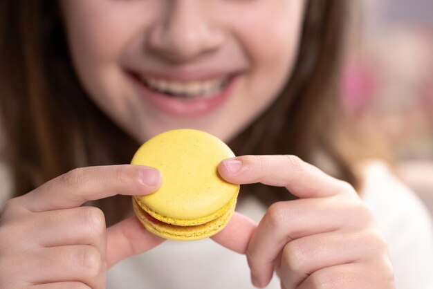 Close up vue de face méconnaissable brunette kid girl mord jaune macaron cookie savoureux couleur douce