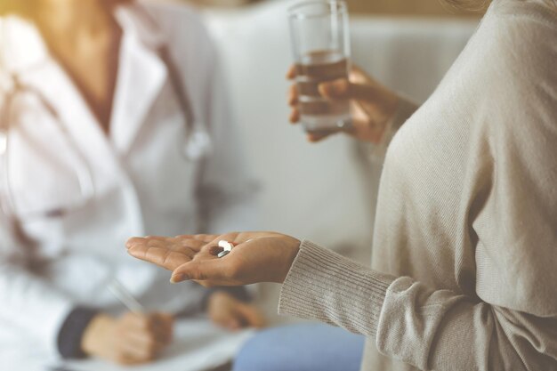 Photo close-up woman-patient holding pills près de son médecin, le temps de prendre des médicaments pour les maux de tête. concept de séjour à la maison pendant la pandémie de coronavirus et la quarantaine d'auto-isolement. covid 2019