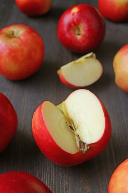 Closeup cut pomme rouge mûre avec de nombreux fruits entiers éparpillés sur une table en bois