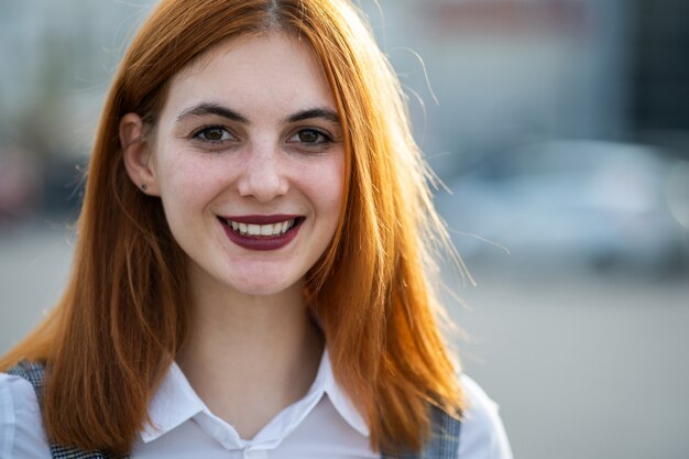 Closeup face portrait of a smiling teenage girl with red hair and clear eyes.