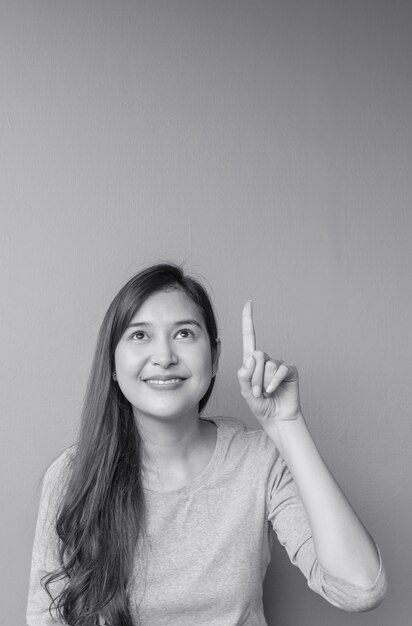 Closeup femme asiatique détient un point de doigt vers l&#39;espace avec le visage de sourire sur le mur de ciment floue fond texturé