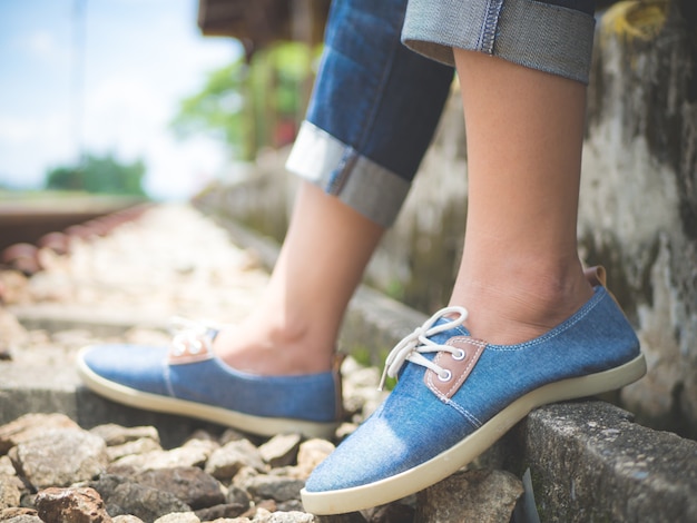 Closeup femme pieds en baskets bleues assis près du chemin de fer.