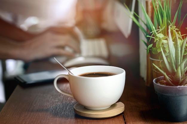 Closeup image de la tasse de café blanche sur teable en bois avec flou image de la main en tapant le clavier de l&#39;ordinateur