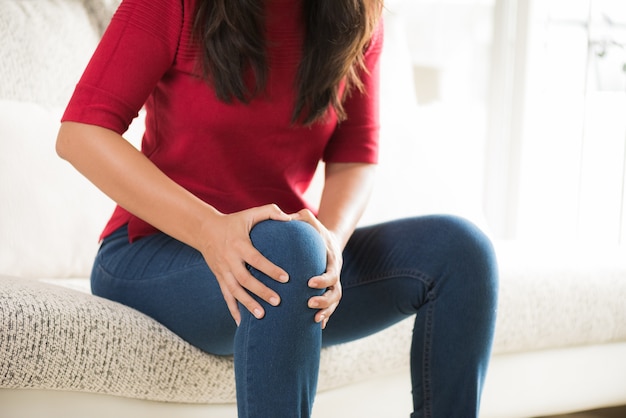 Closeup jeune femme assise sur le canapé et sensation de douleur au genou