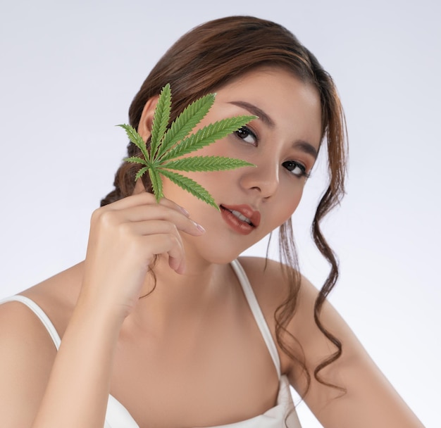 Closeup magnifique femme avec une peau fraîche saine et cosmétique tenant une feuille de chanvre