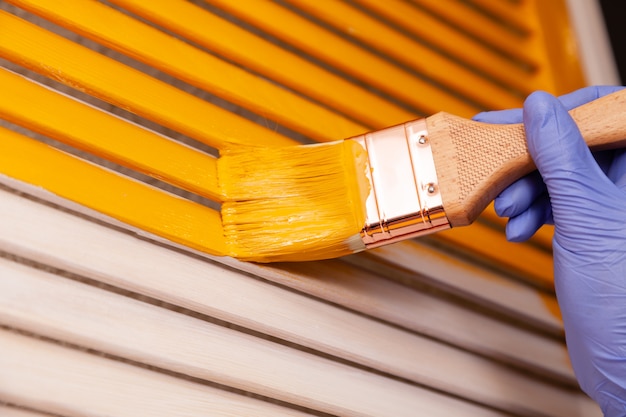 Closeup main féminine dans un gant en caoutchouc violet avec porte en bois de peinture au pinceau avec de la peinture orange. intérieur coloré créatif design créatif. Comment peindre une surface en bois. Focus sélectionné